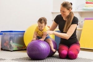 Occupational Therapy Assistant helping a small child use an exercise ball